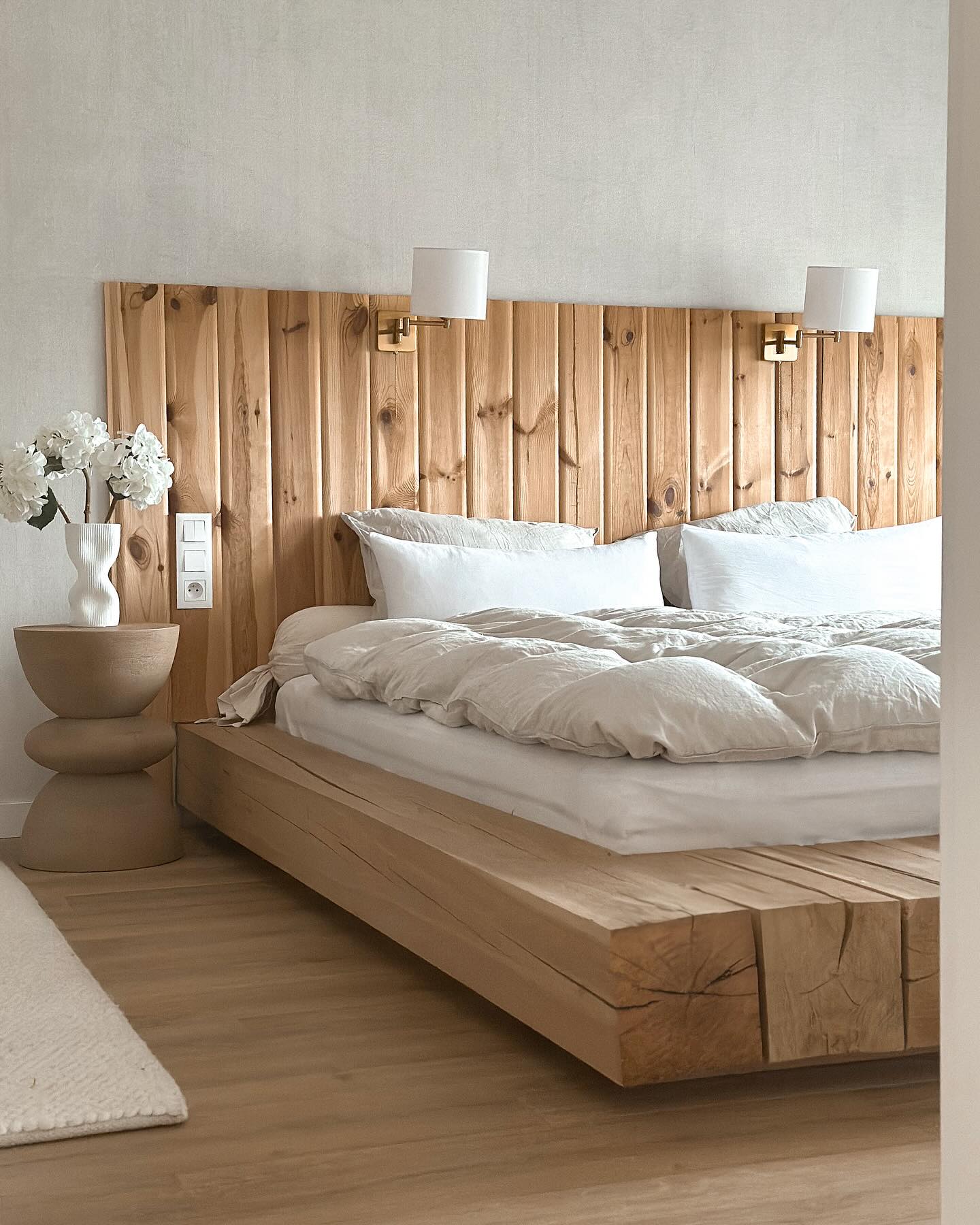 Bedroom with platform bed made of light wood, white bedding, and wooden headboard.