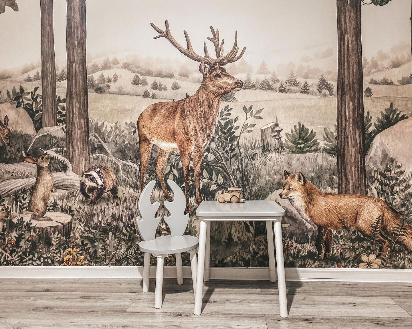 Child's gray table and deer-antler chair against a woodland animal wallpaper.