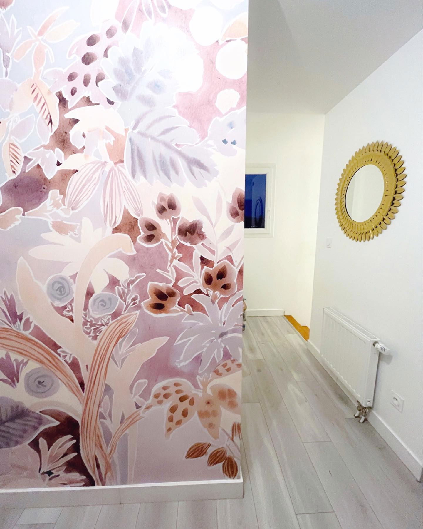 Pasillo con papel tapiz floral, pisos de madera y un espejo dorado con forma de sol.