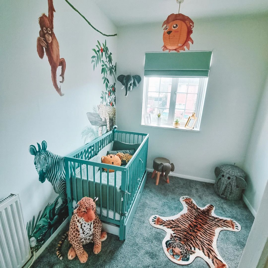 Børneværelse med jungletema, med en blå tremmeseng, dyrevægdekorationer og tigergulvtæppe.