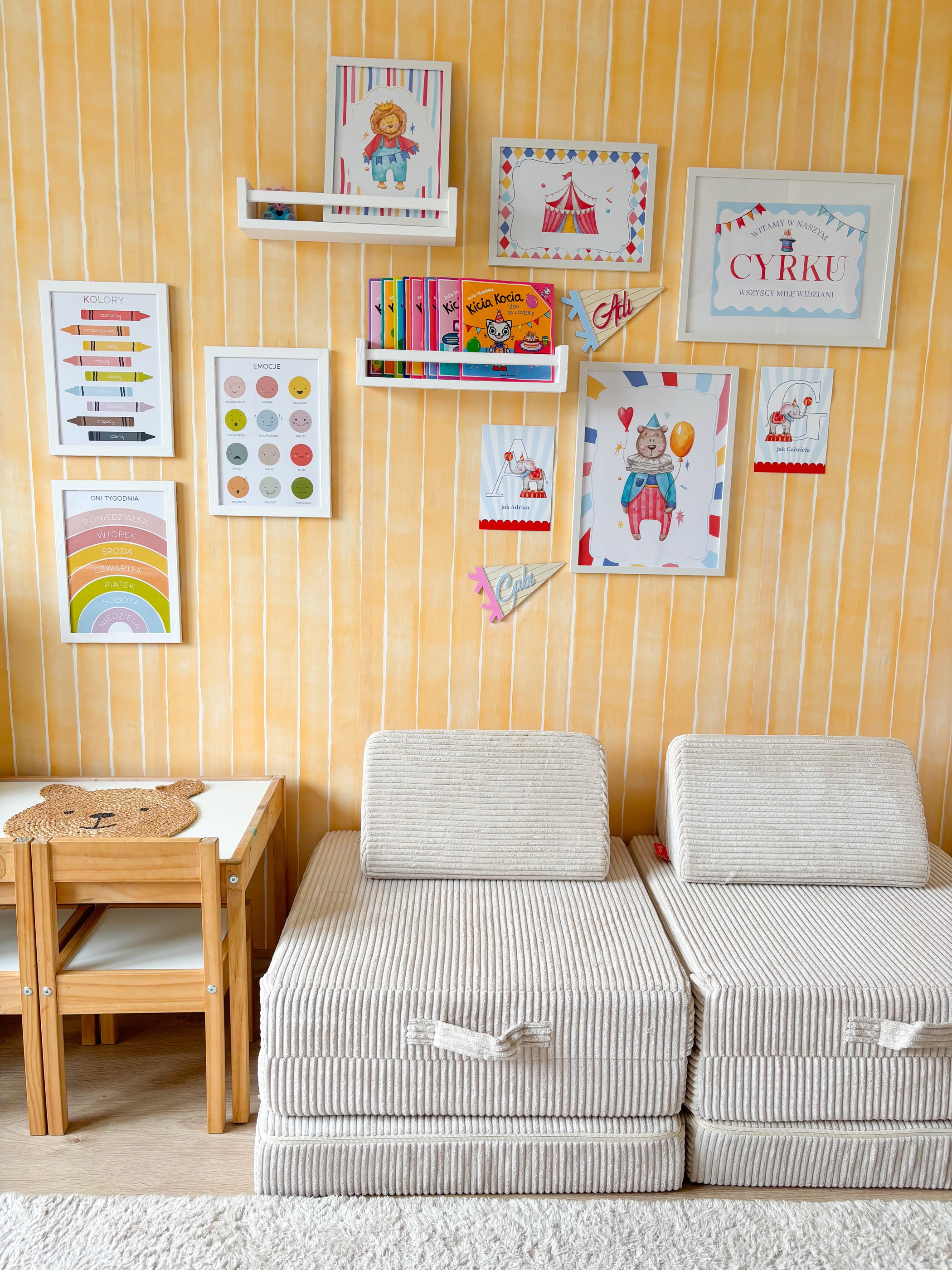 Yellow striped playroom walls display framed art and books. Two light beige corduroy floor chairs, a small wooden table with chairs.
