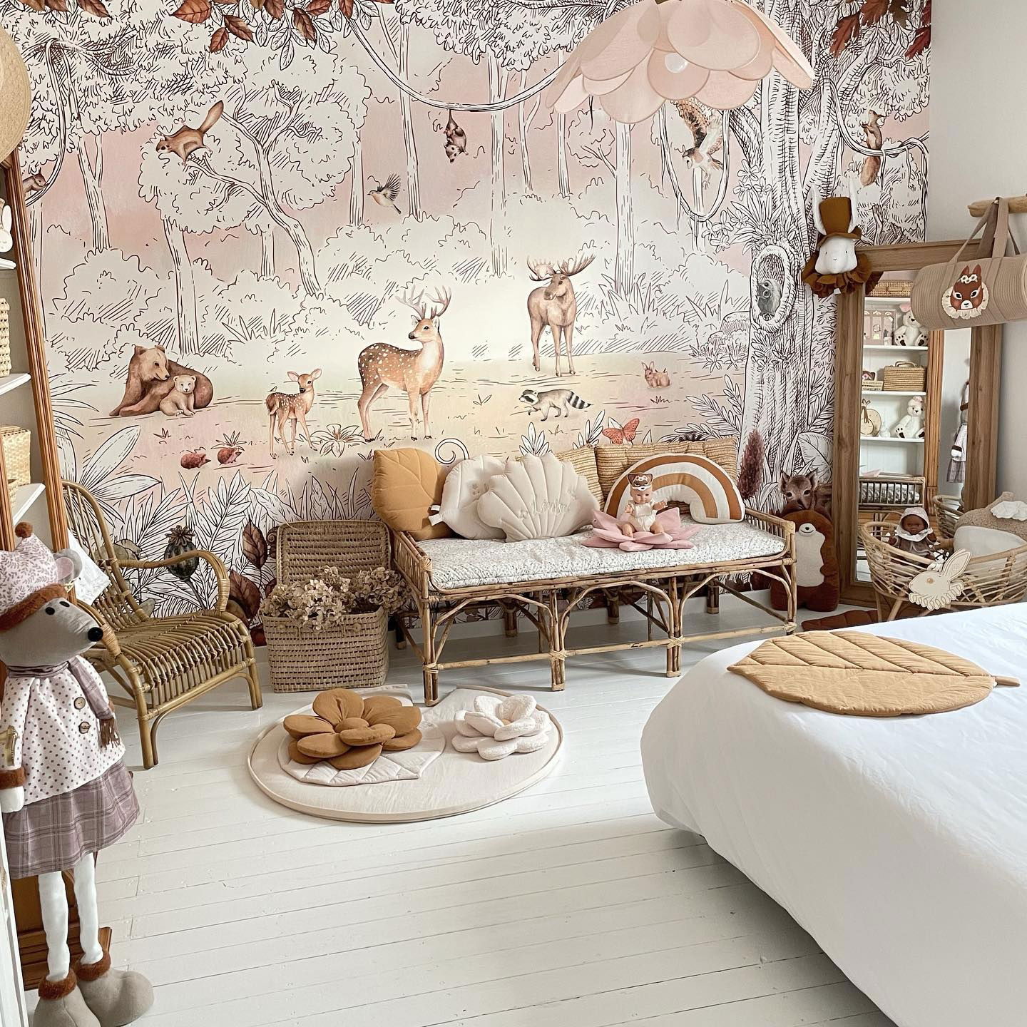 Whimsical nursery with forest-themed wallpaper, rattan furniture, and plush toys.