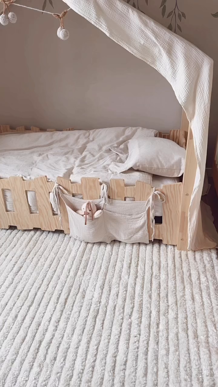 Child's bed with light wood frame, white muslin canopy, and storage bag with stuffed bunny.