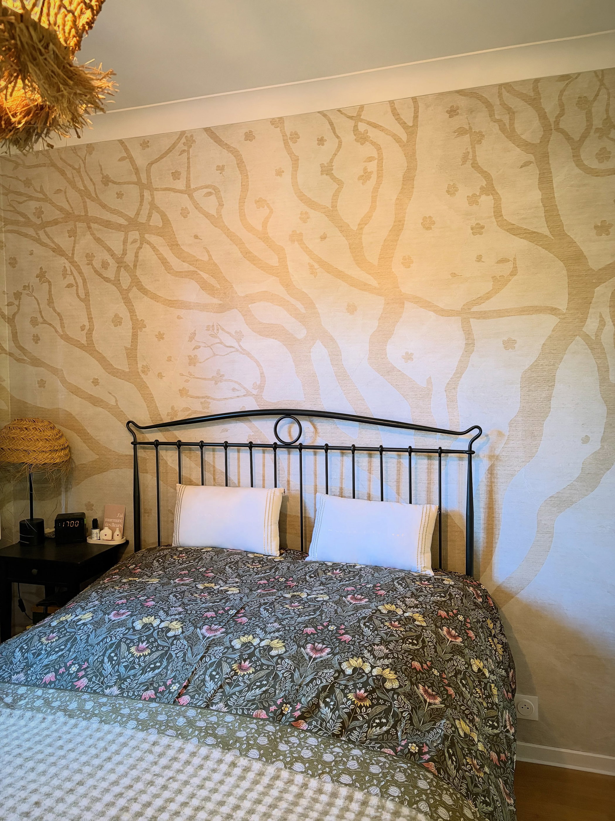 Bedroom with a floral duvet, white pillows, and a tree-patterned wallpaper.