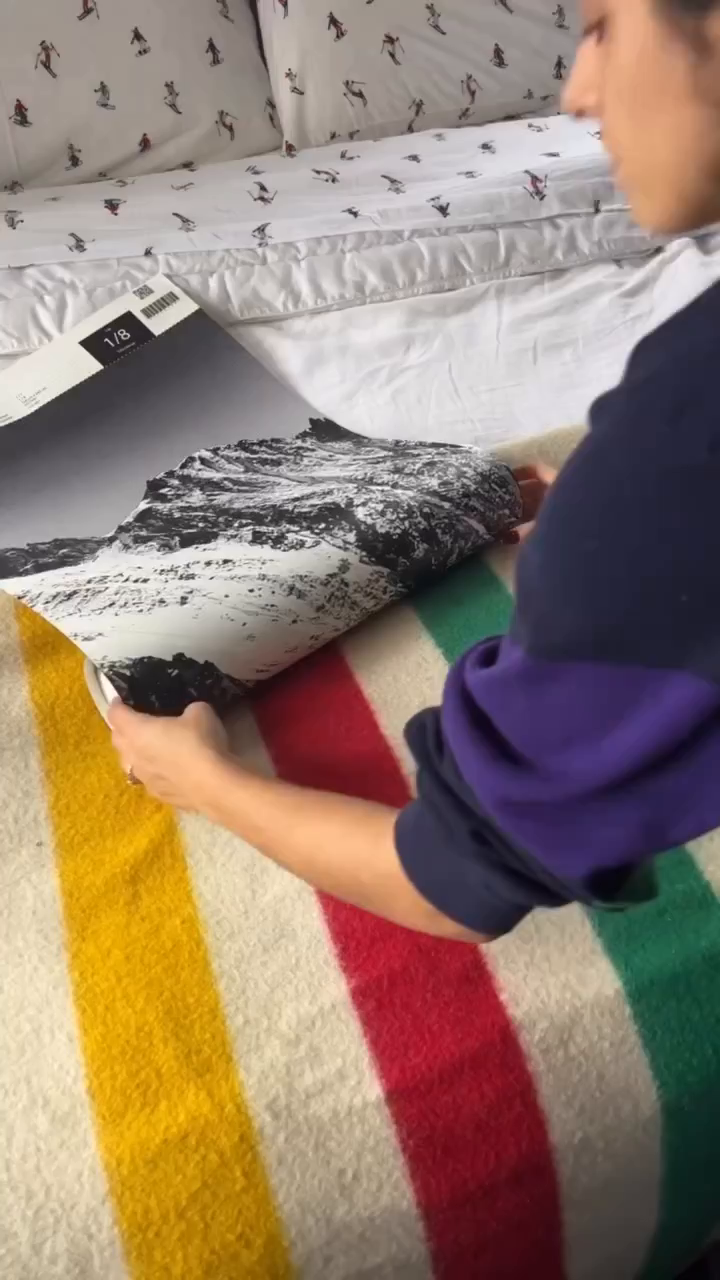 Person holding a black and white mountain print over a striped blanket.