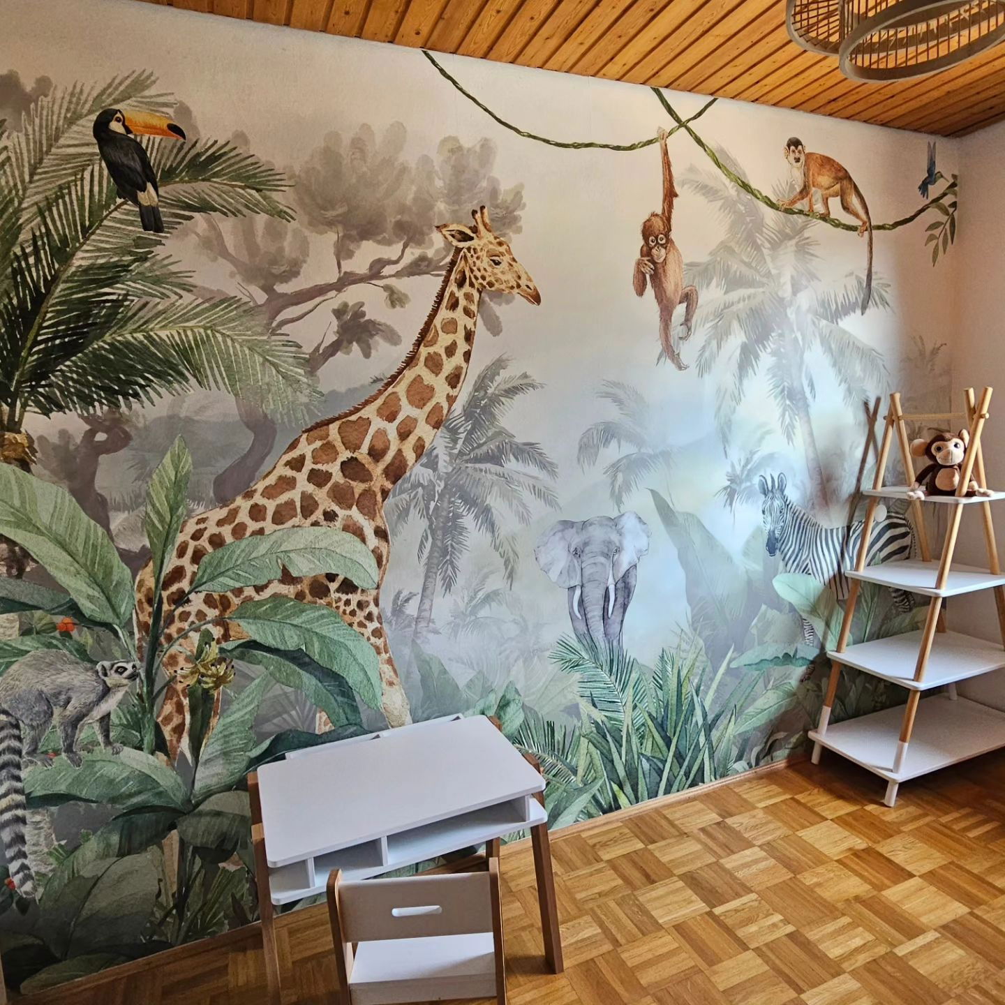 Kinderzimmer mit Dschungel-Wandbild mit Giraffe, Affen, Tukan, Elefant und Zebra.