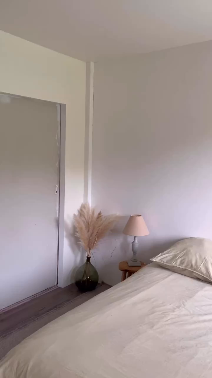 Bedroom with bed, nightstand, lamp, and pampas grass in a green vase.