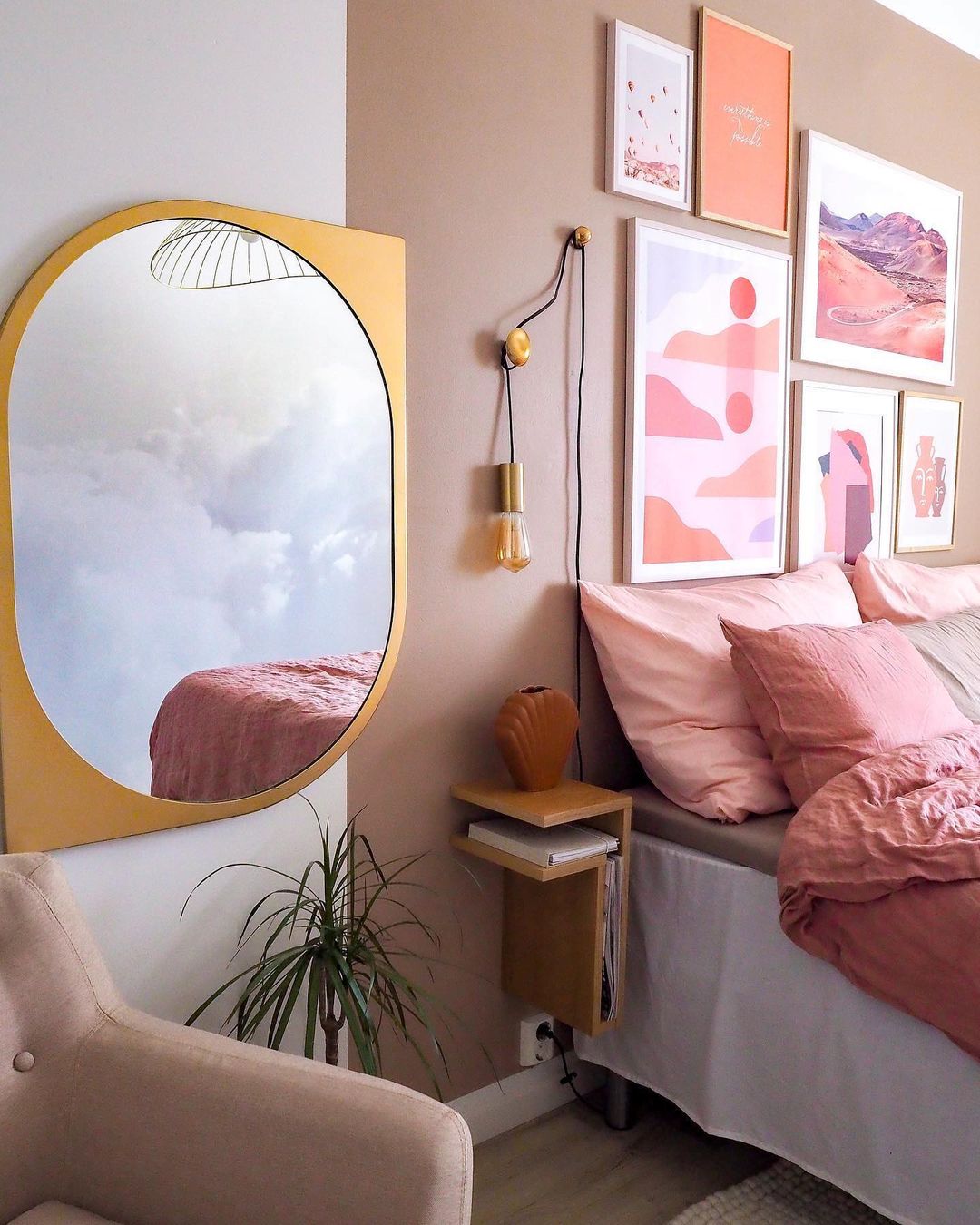 Cozy bedroom with pink bedding, gallery wall, and gold-framed mirror reflecting clouds.