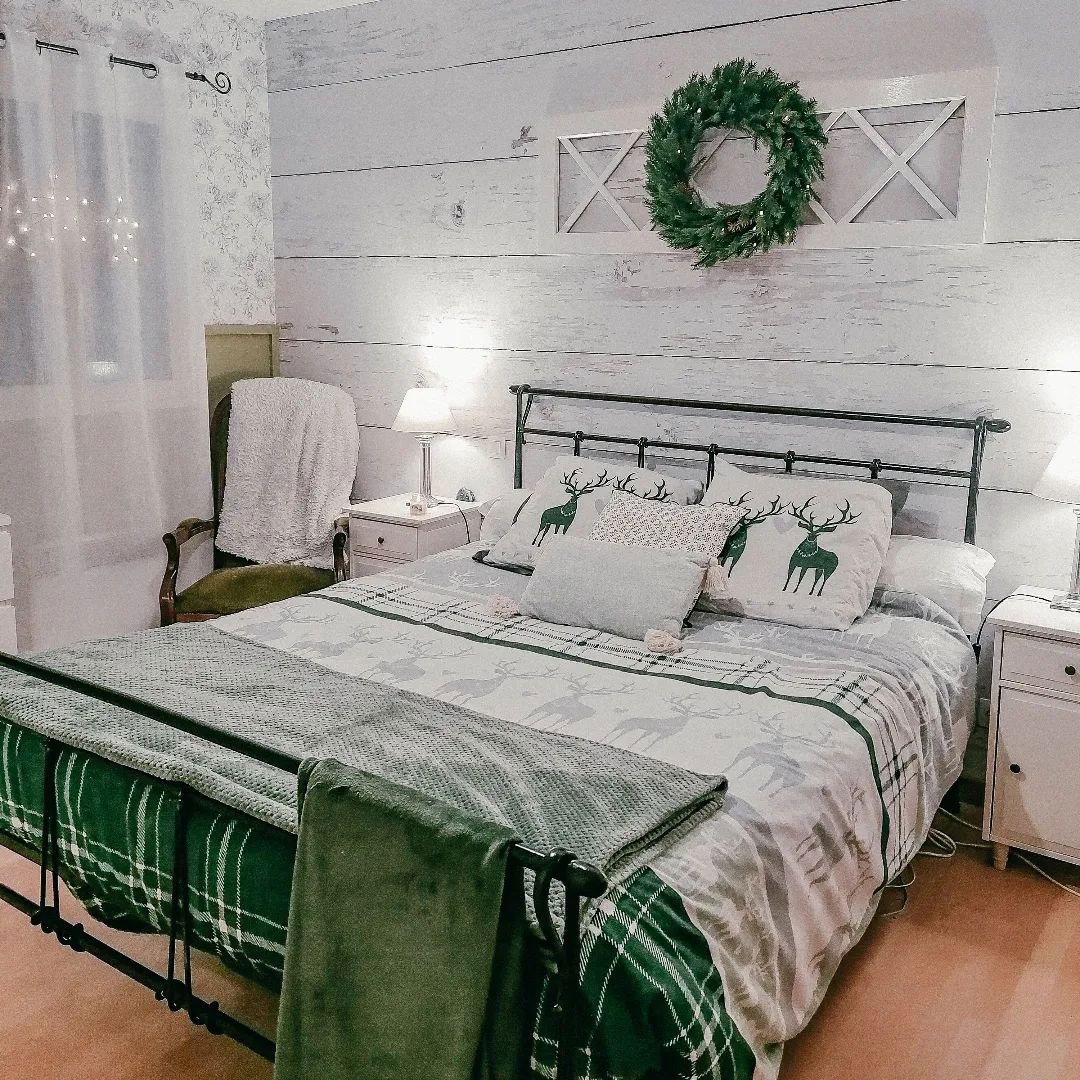 Slaapkamer met ijzeren bedframe, beddengoed met hertenthema en een krans boven het hoofdeinde.