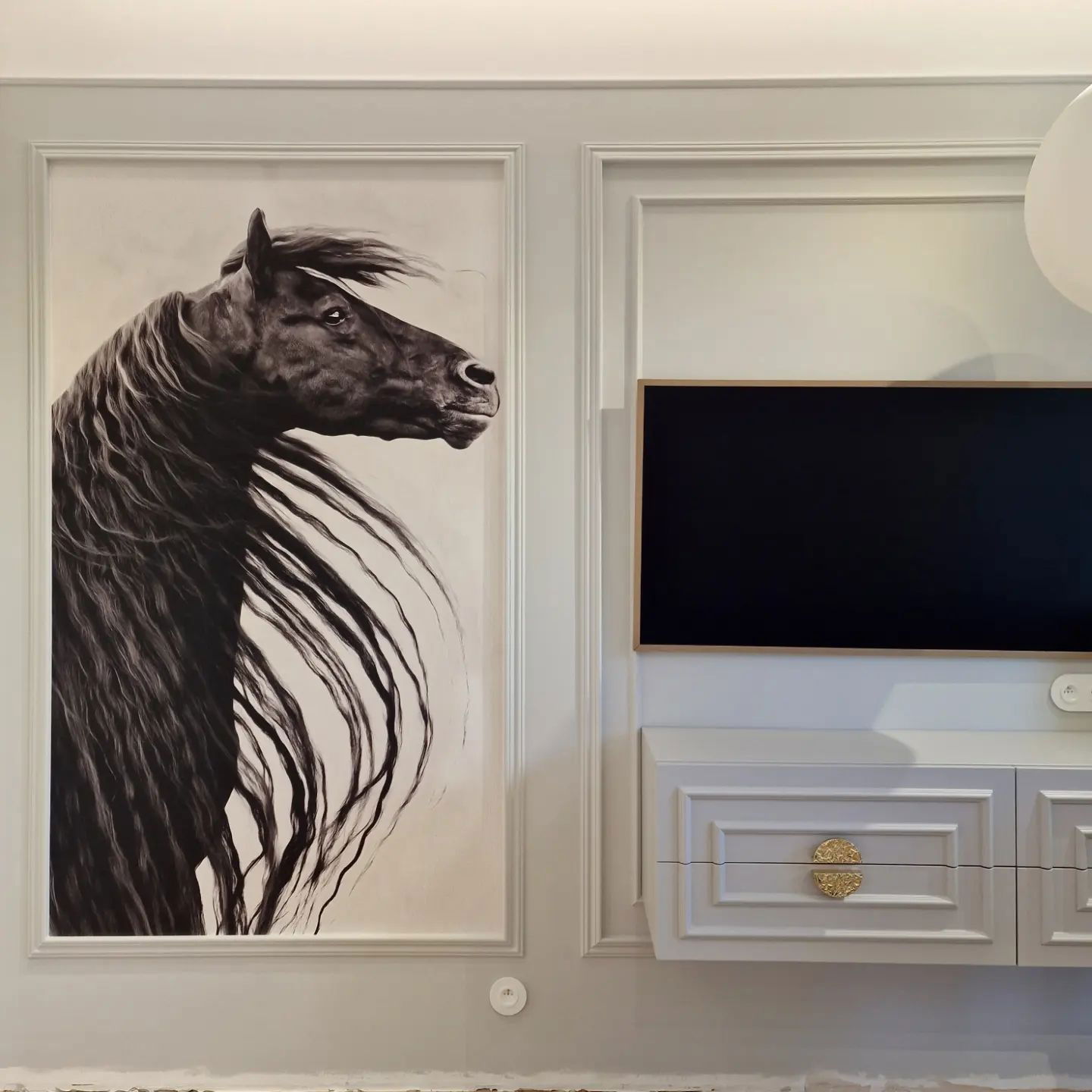 Living room wall with framed horse art, TV, and white cabinet.