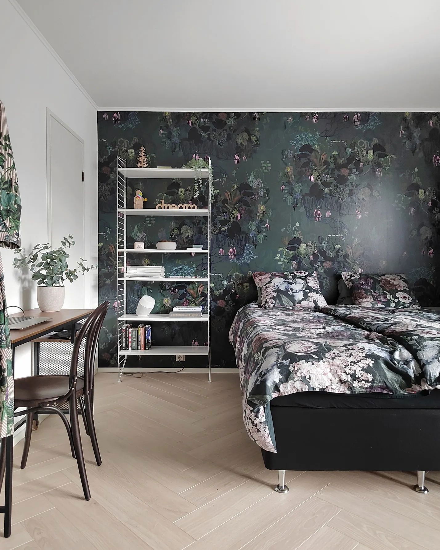 Bedroom with floral wallpaper, bed with floral bedding, white shelving unit, and desk with chair.