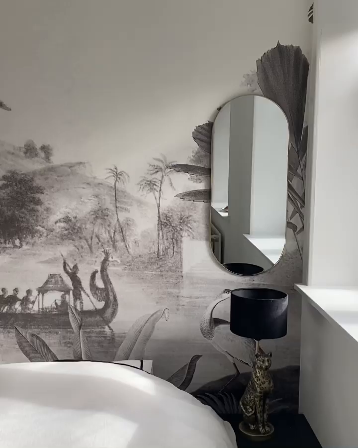Bedroom with tropical mural, oval mirror, and black lamp with leopard base.