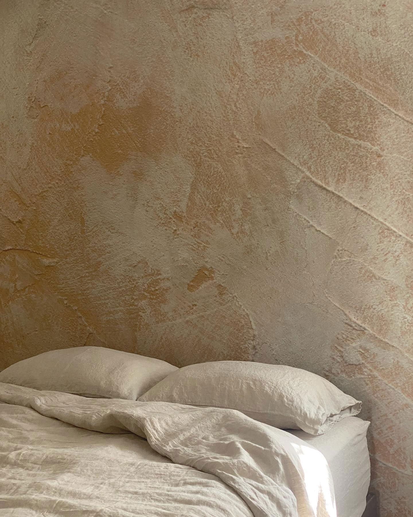 Beige linen bedding with pillows against a textured, painted wall.