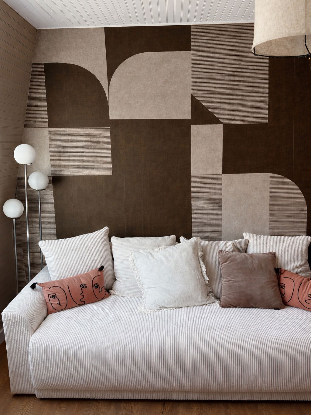 White corduroy sofa with plush pillows and a graphic brown and beige wallpaper backdrop.