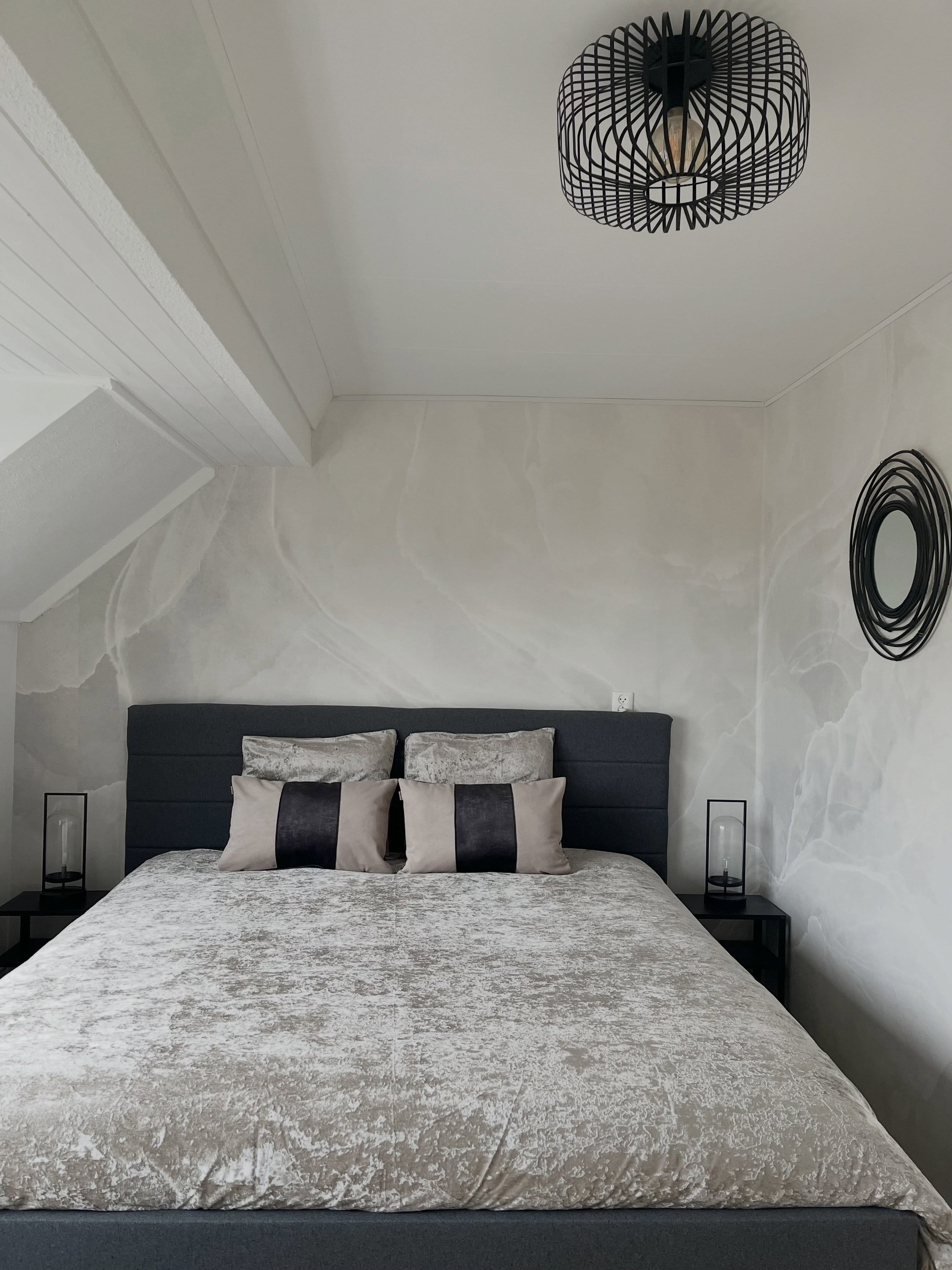 Stylish bedroom with a king-sized bed, dark headboard, textured bedding, and marble-patterned walls.