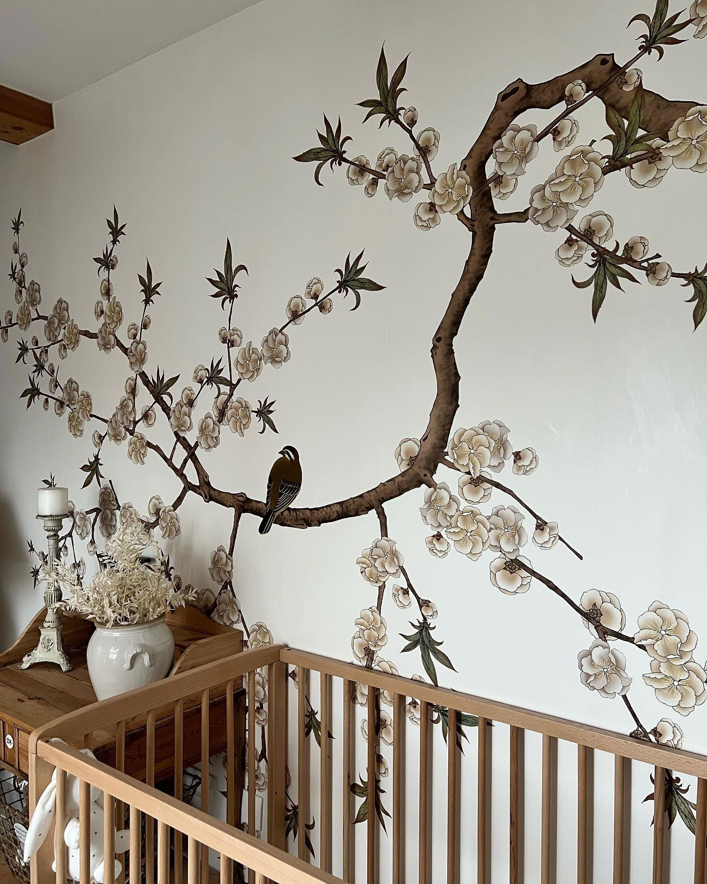 Babykamer met bloemenmuurschildering, vogel en houten wieg. Links staat een vintage houten dressoir.