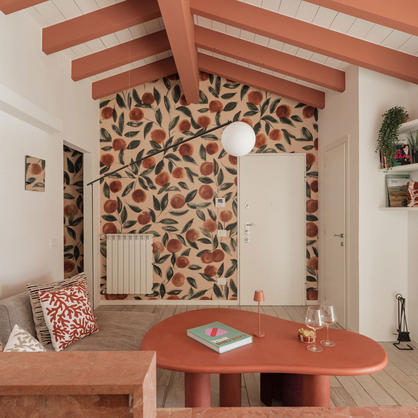 Living room with orange fruit wallpaper, beams, and a kidney-shaped coffee table.