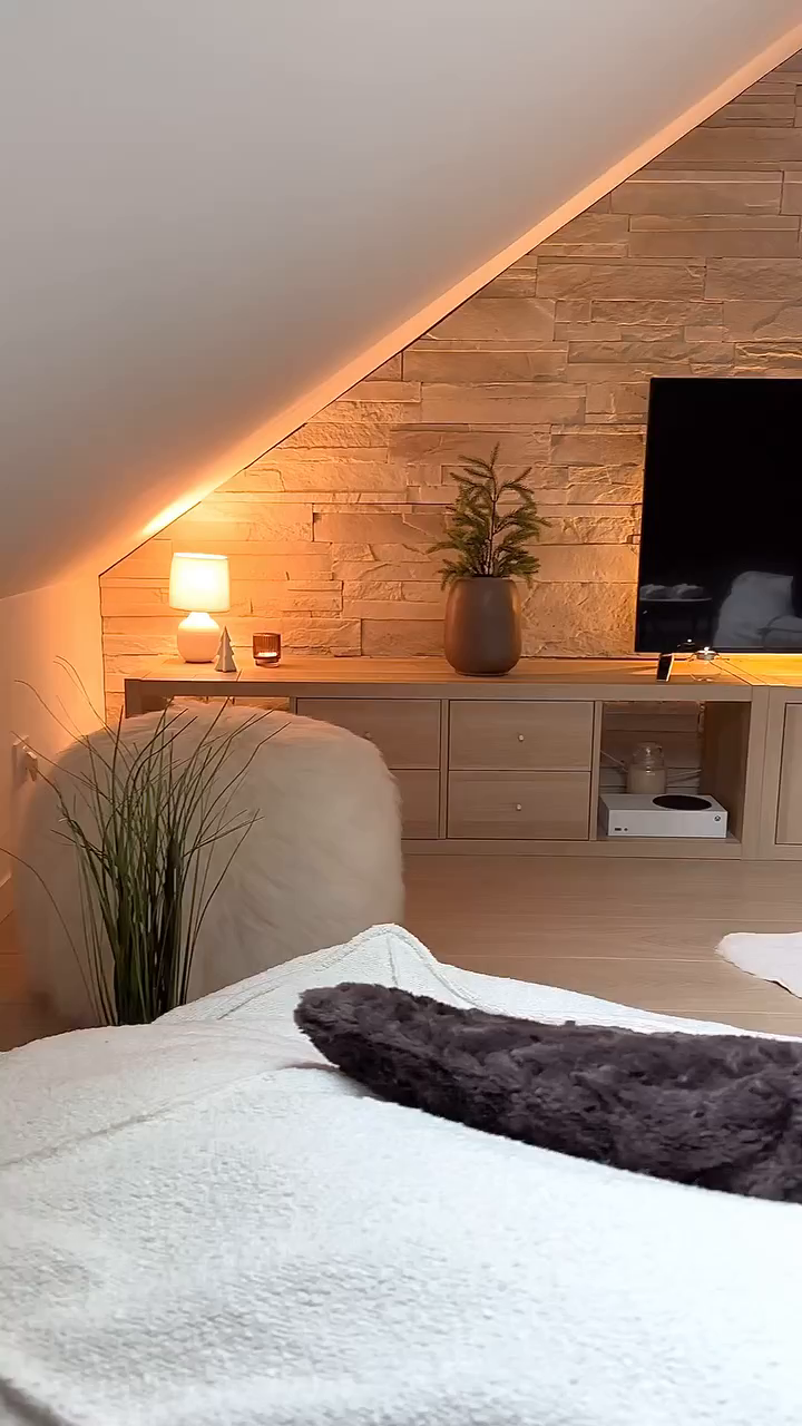 Cozy living room with TV, stone wall, and white faux fur ottoman.
