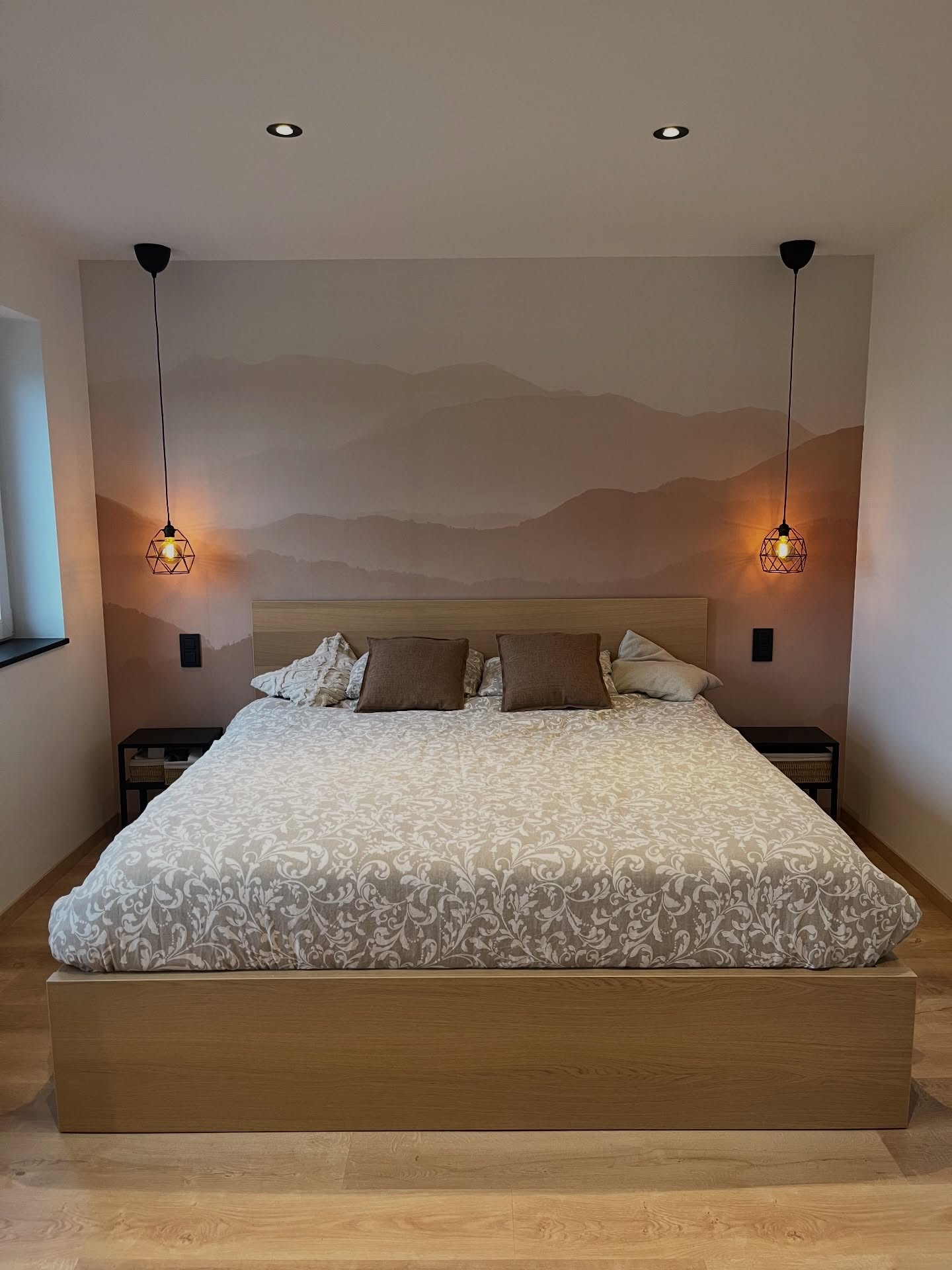 Moderne slaapkamer met een houten platformbed, een dekbed met patroon en een muurschildering van bergen.