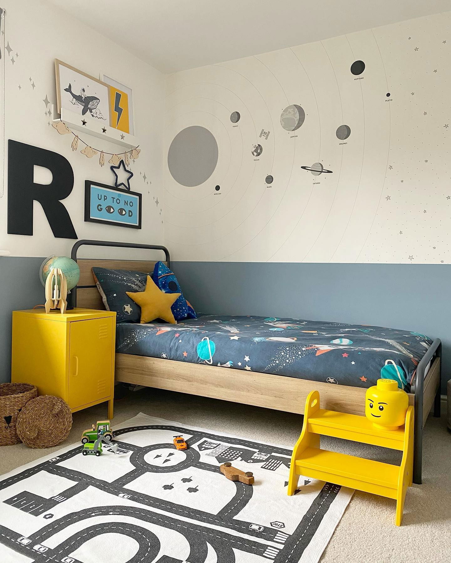 Child's bedroom with space theme, featuring a road rug, yellow accents, and planet wall decals.