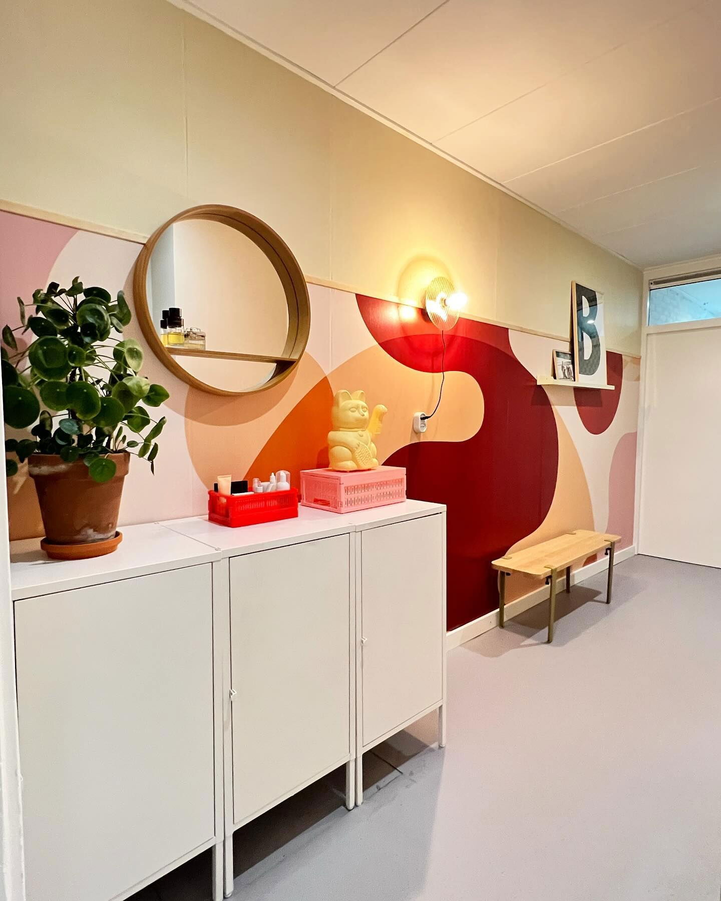 Gang med hvite skap, rundt speil og fargerik abstrakt veggkunst.