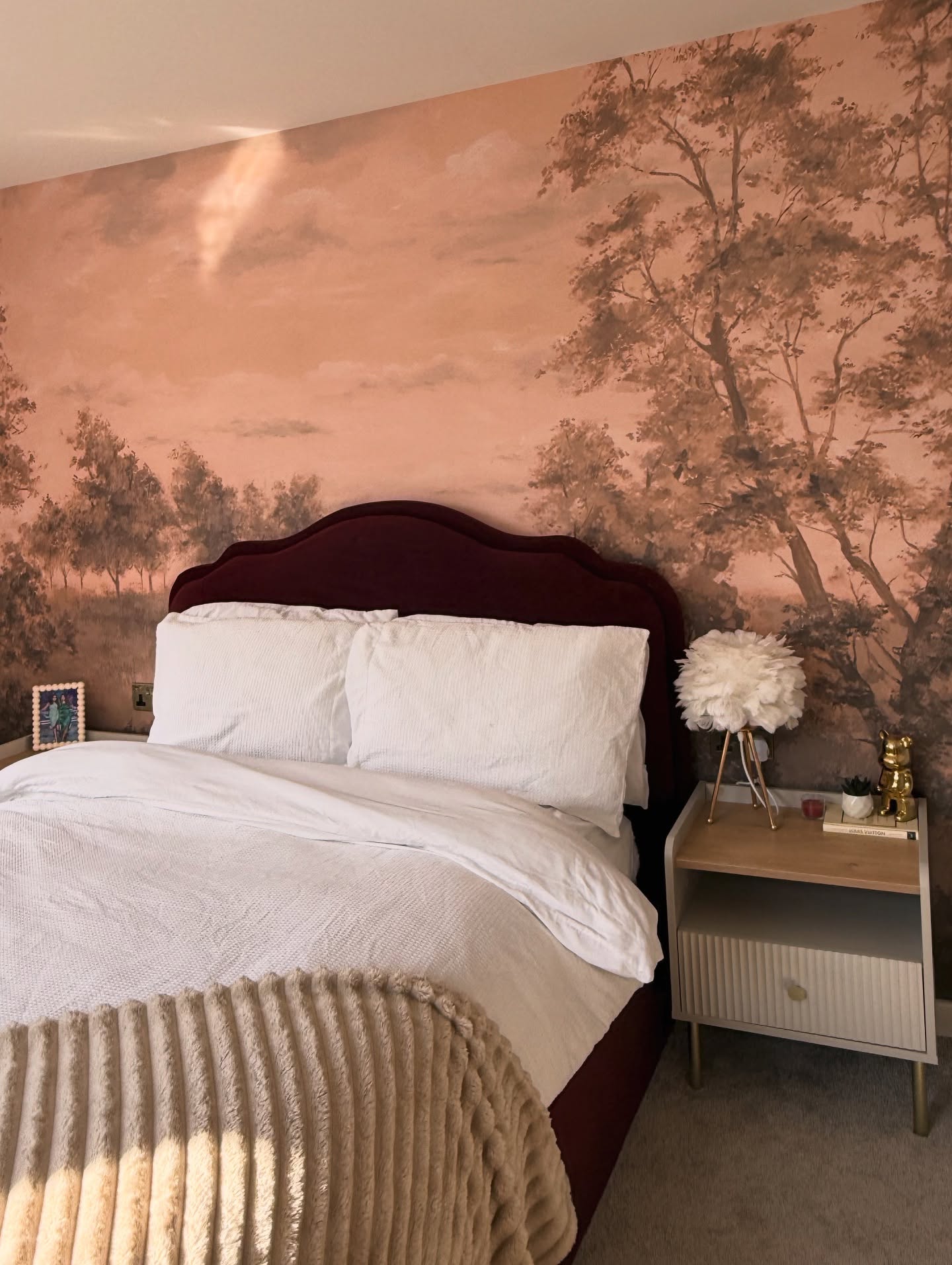 Bedroom with red headboard, white bedding, and landscape mural. Nightstand with lamp and decor.