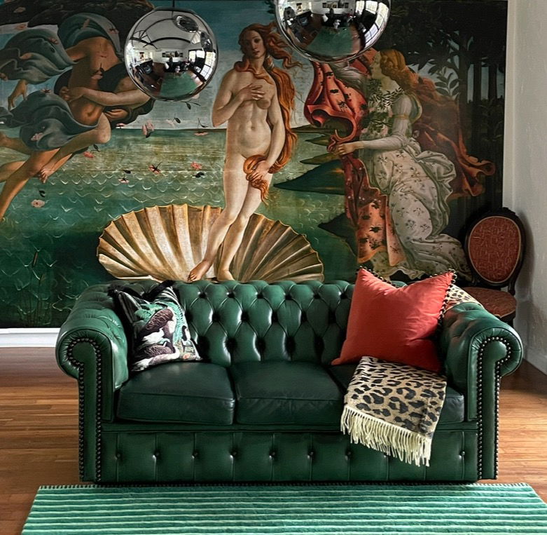 Living room with green leather sofa, "Birth of Venus" backdrop, and mirrored disco balls.