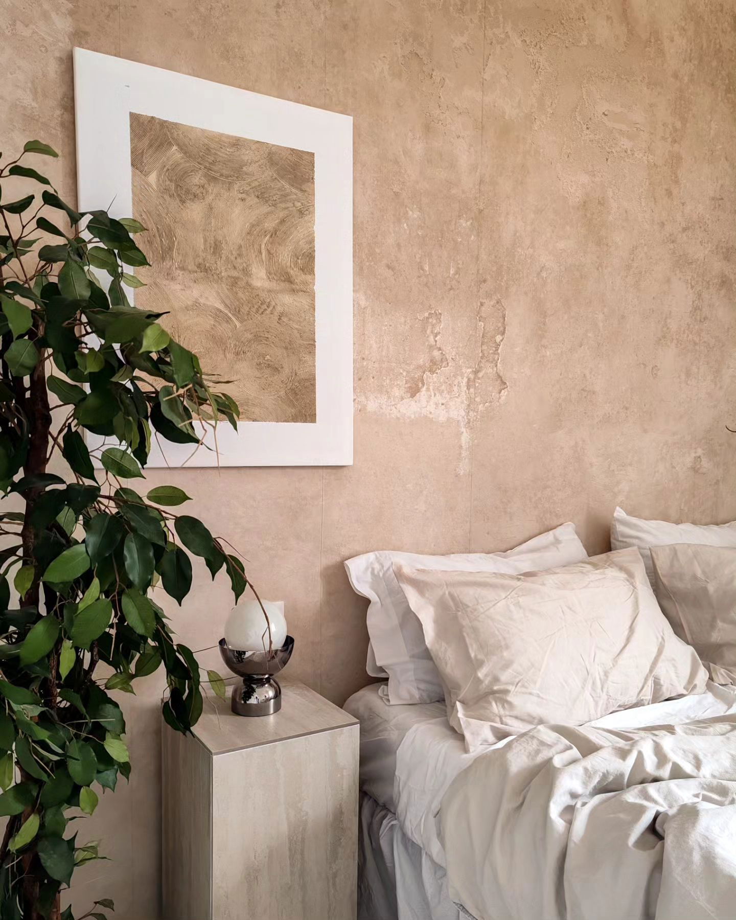 Schlafzimmerecke mit Bett, Nachttisch, Pflanze und gerahmter Kunst.