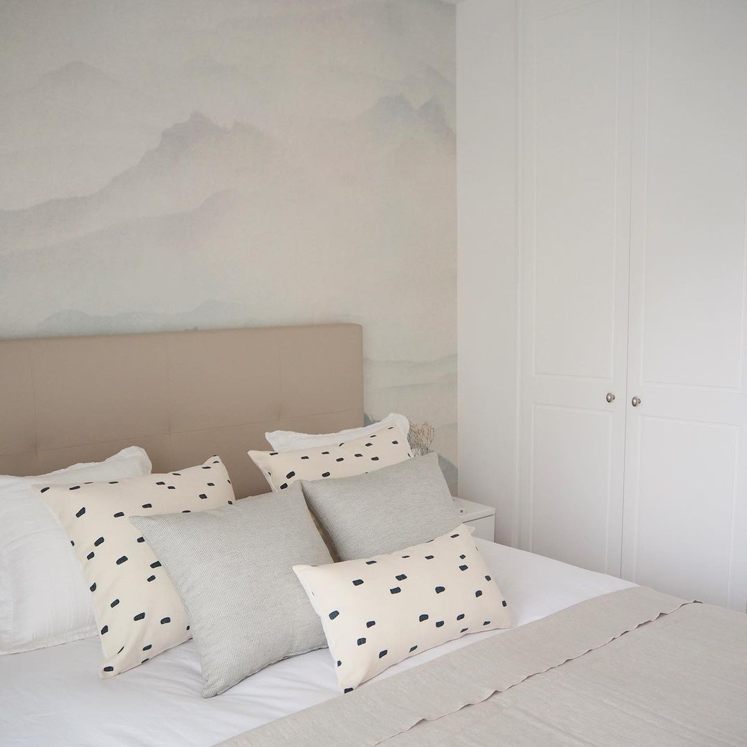 Soveværelse med beige sengegavl, hvidt sengetøj og puder. Bjergmaleri på væggen.