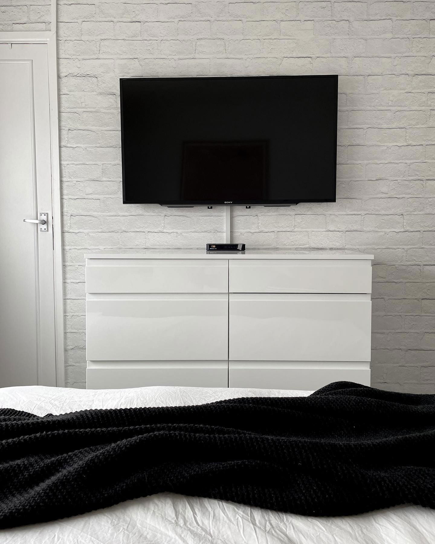 Bedroom with Sony TV mounted above a white dresser, black blanket on bed.