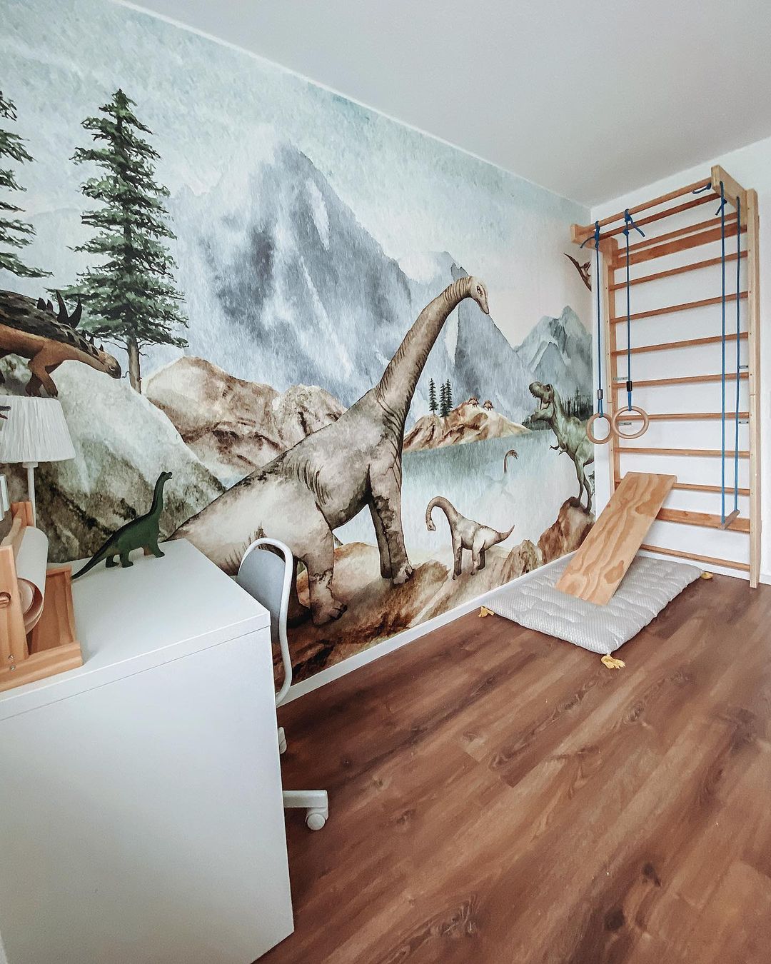 Child's room with dinosaur wallpaper, white desk, and wooden climbing wall.