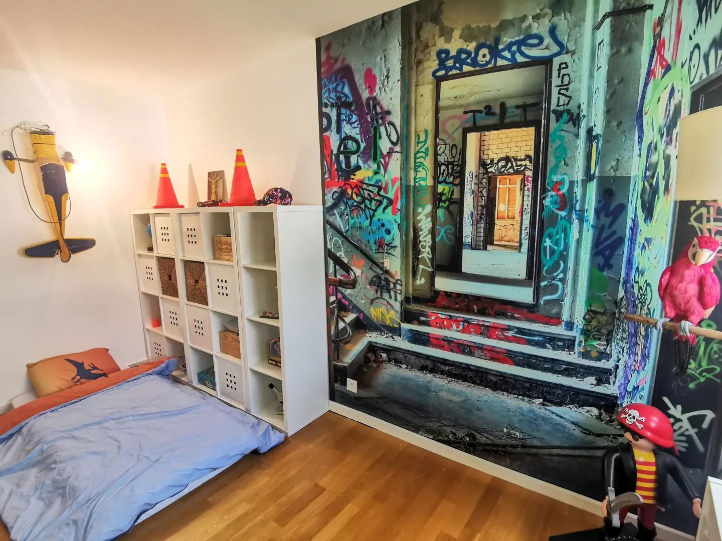 Child's room with floor bed, white cube storage, and graffiti-style wall mural.