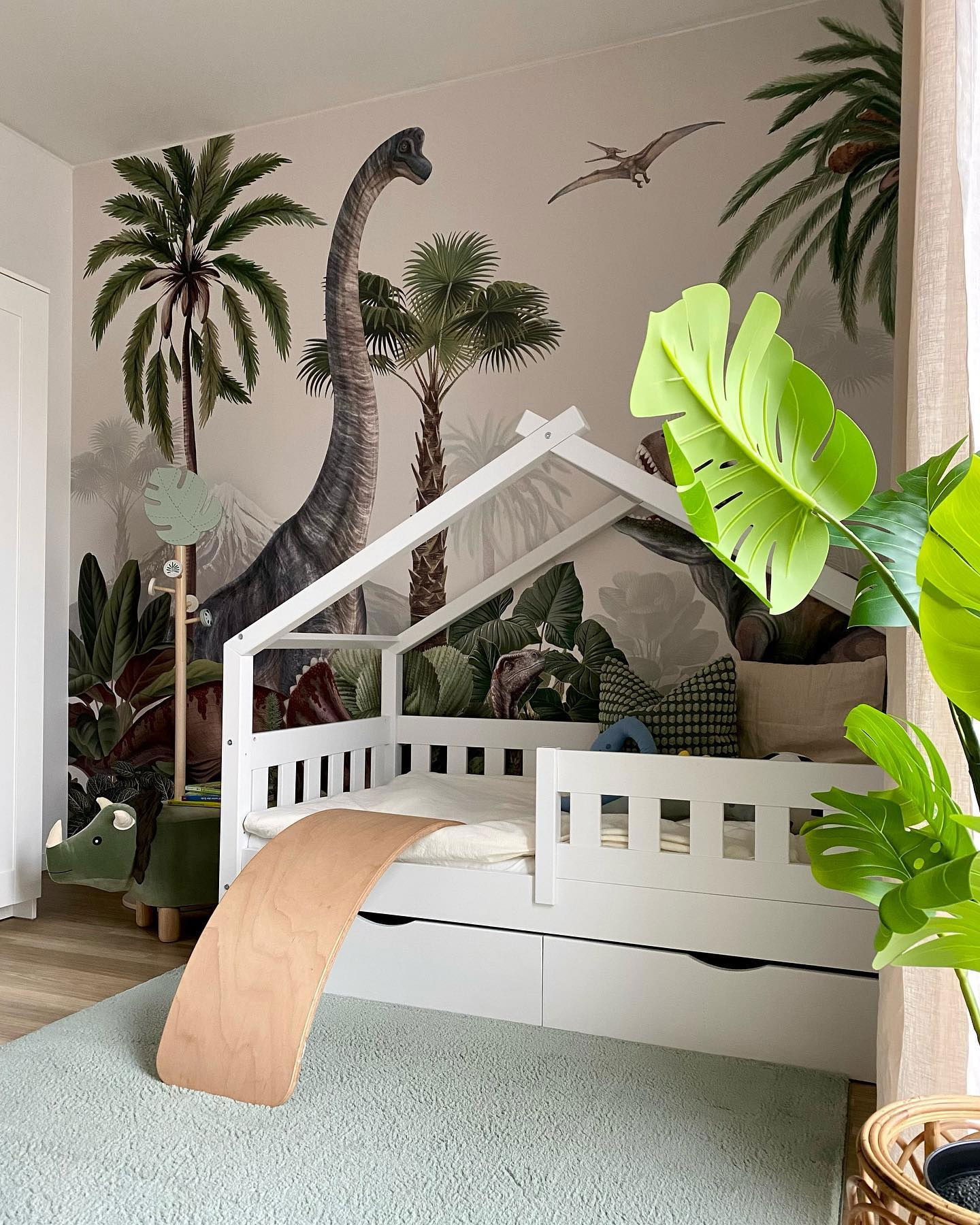 Child's bedroom with dinosaur wallpaper, white house-frame bed, and wooden balance board.