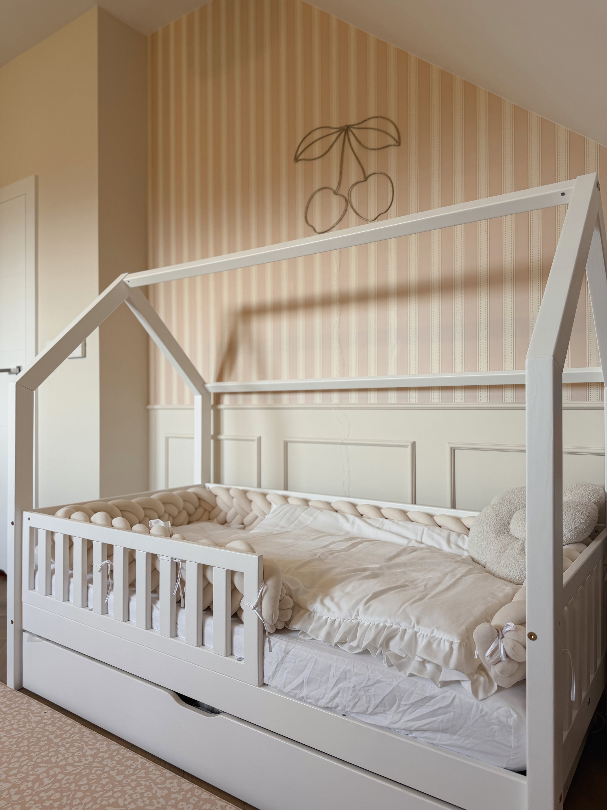 White house-shaped toddler bed with drawer and a braided bumper.