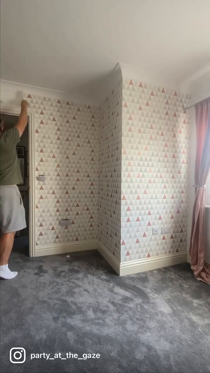 A person applying geometric triangle wallpaper in a room with gray carpet.