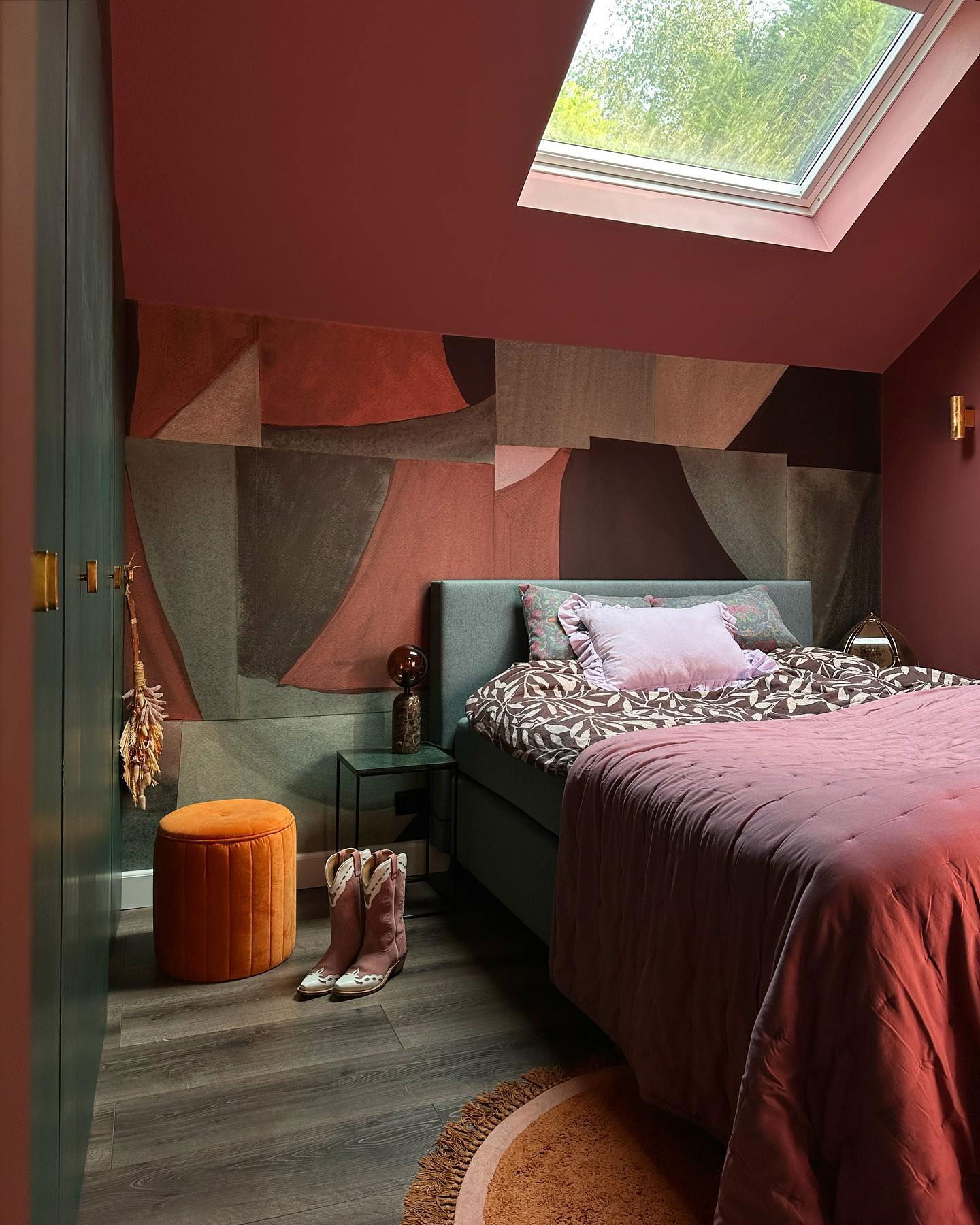 Dormitorio ecléctico con paredes de color óxido, mural geométrico y tragaluz.