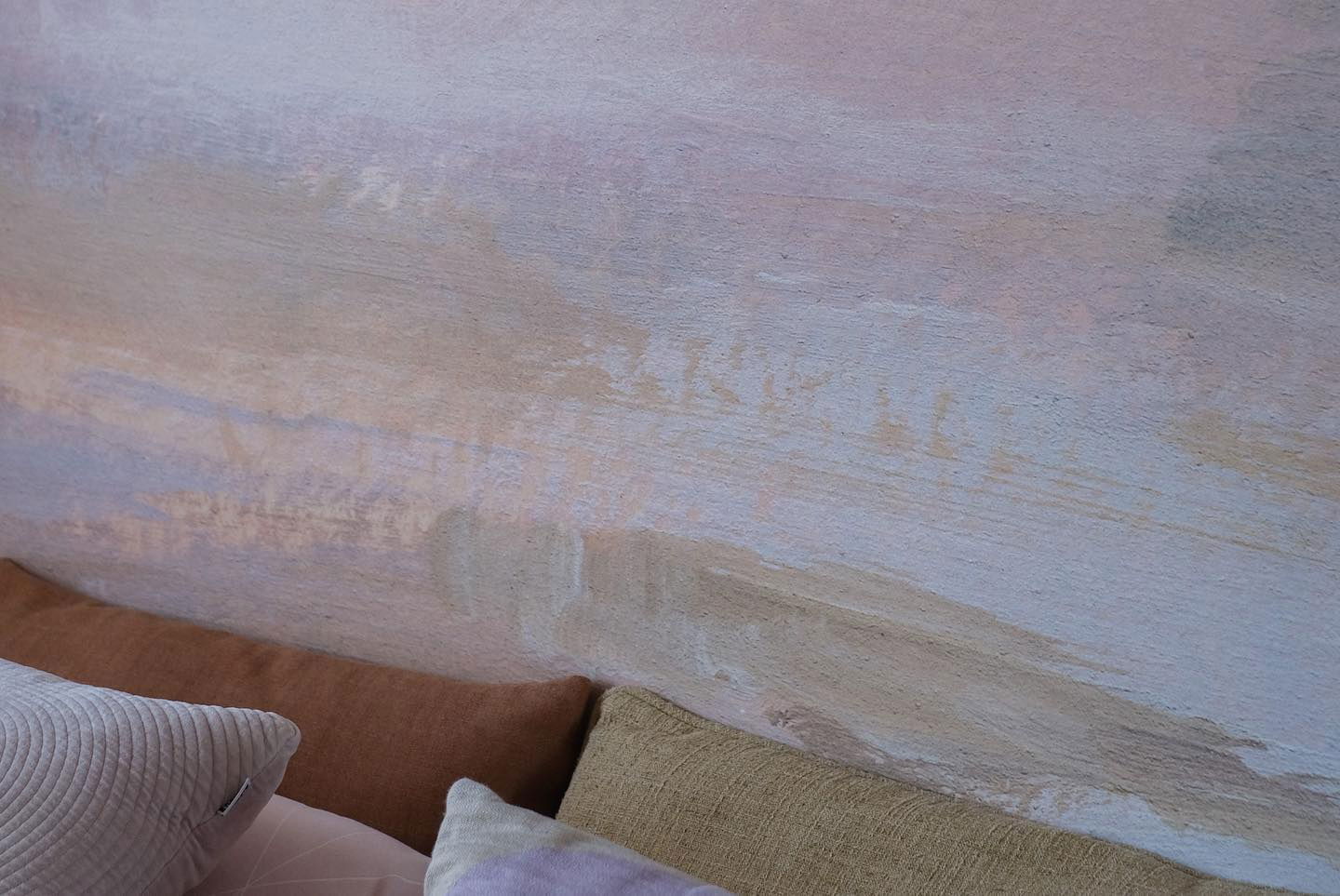 Nærbillede af tekstureret væg med puder i brun, beige og lavendel.