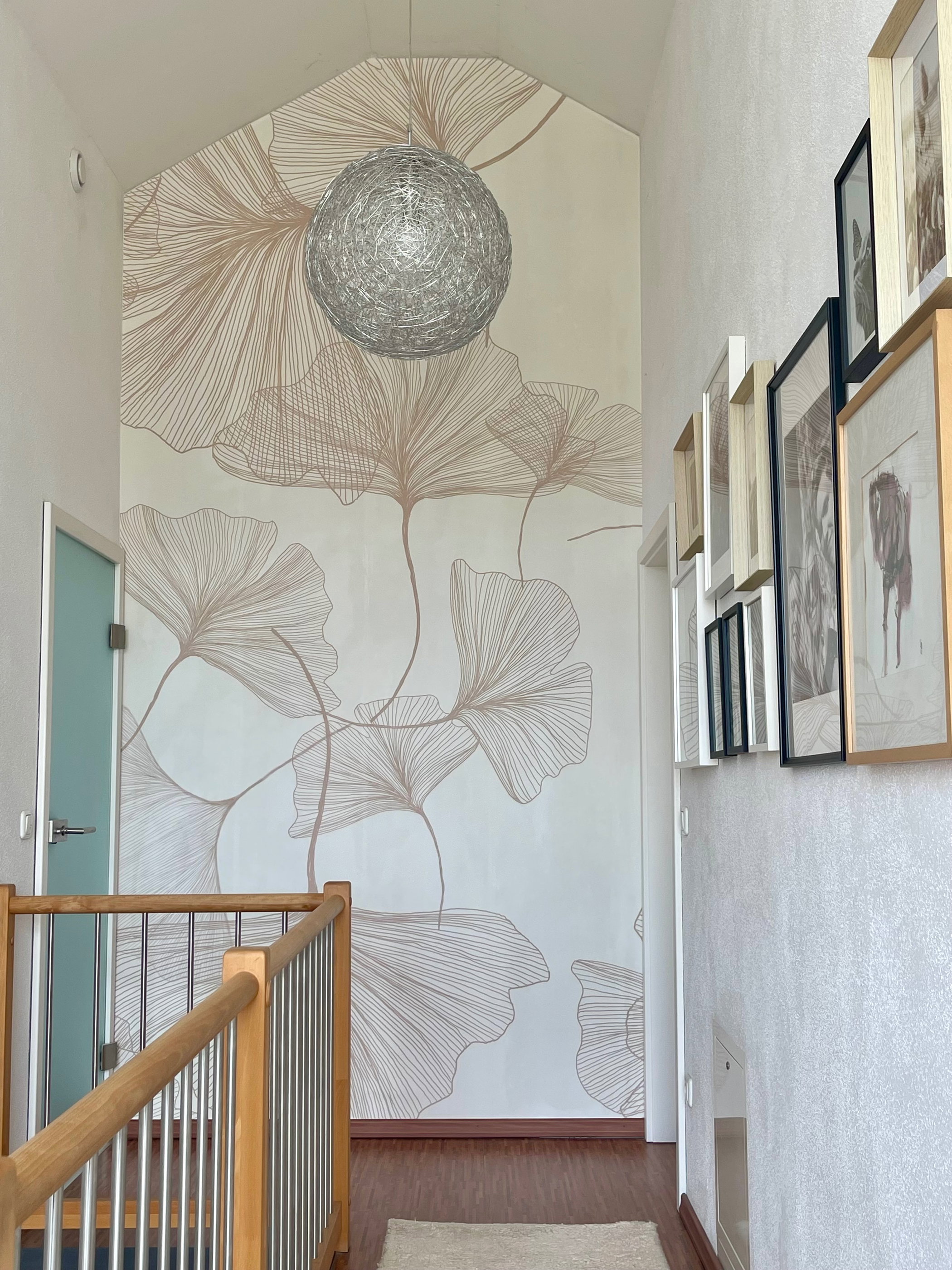 A wall with brown ginkgo leaf wallpaper, a silver spherical light, and a wooden railing in the foreground.