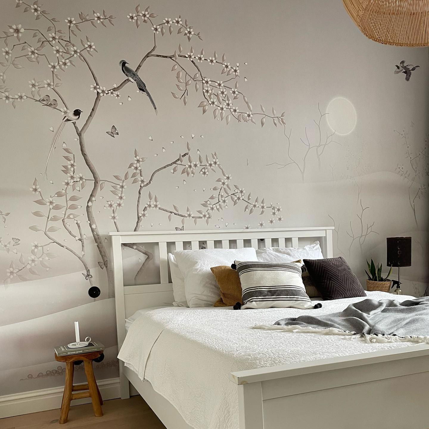 Chambre avec lit blanc, coussins à motifs et une murale représentant des oiseaux et des branches fleuries.