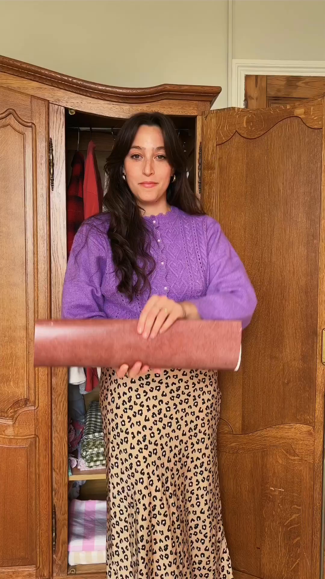 A woman in a purple cardigan and leopard print skirt holds a roll of brown paper.