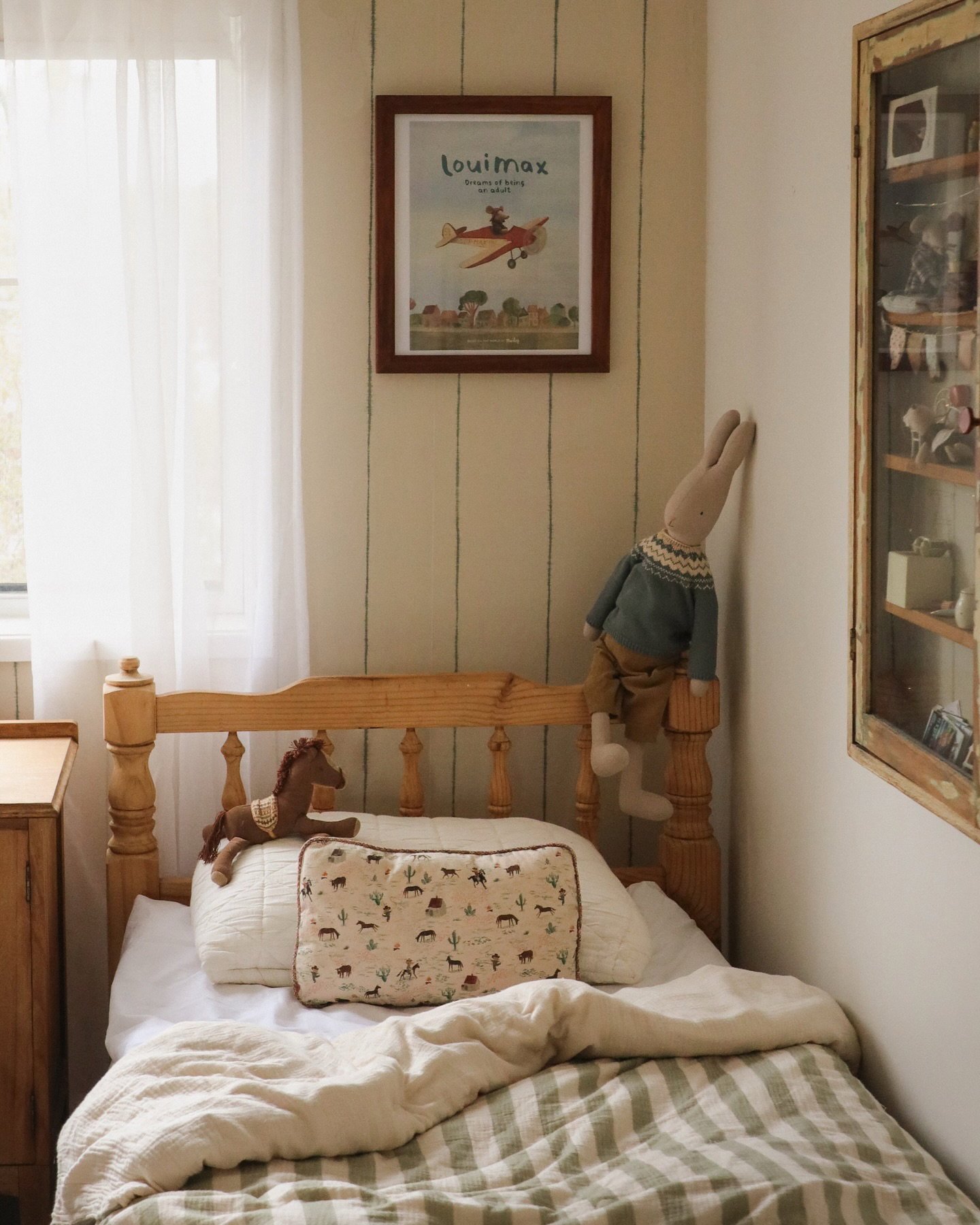 A child's bed with a stuffed bunny hanging off the headboard and a framed airplane print on the wall.