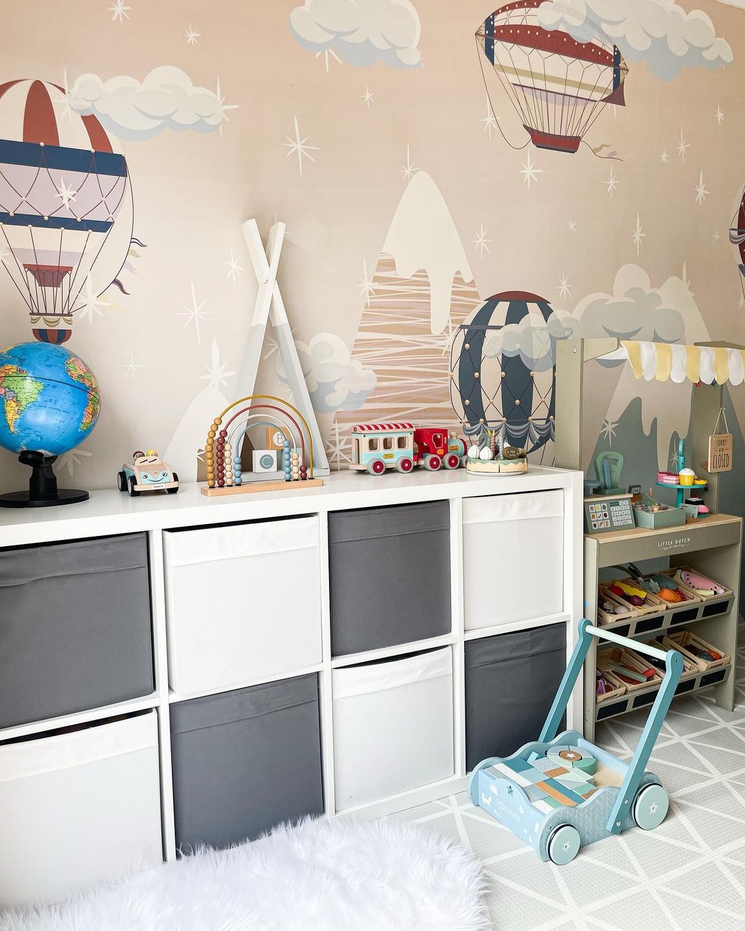 Child's room with hot air balloon wallpaper, white shelving unit with gray and white storage bins, and various toys.