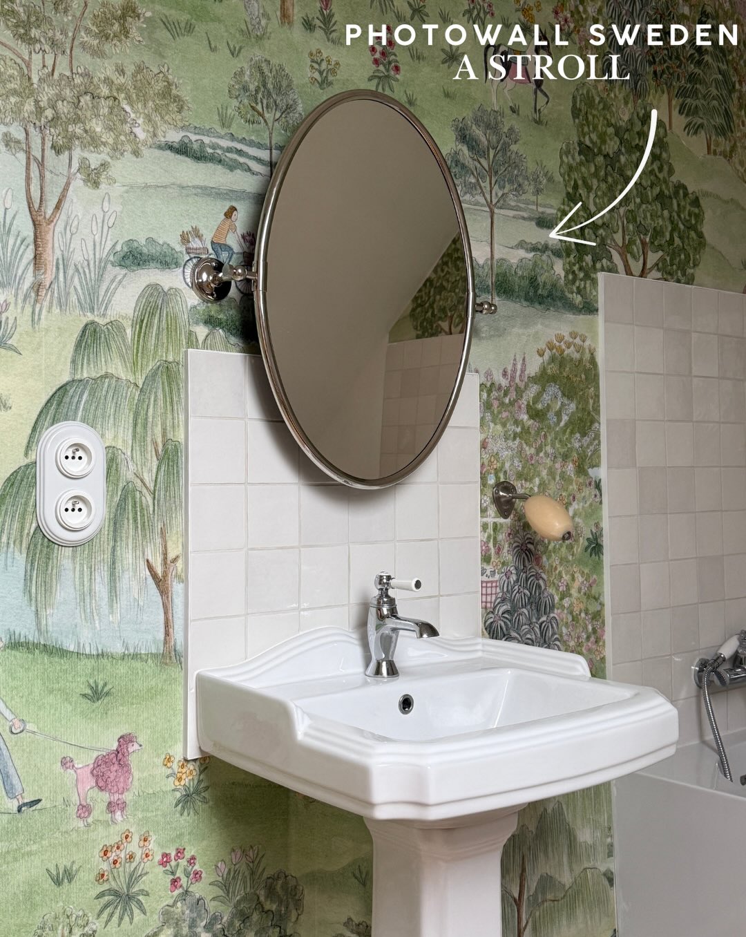 Pedestal sink and oval mirror against a whimsical woodland scene wallpaper.