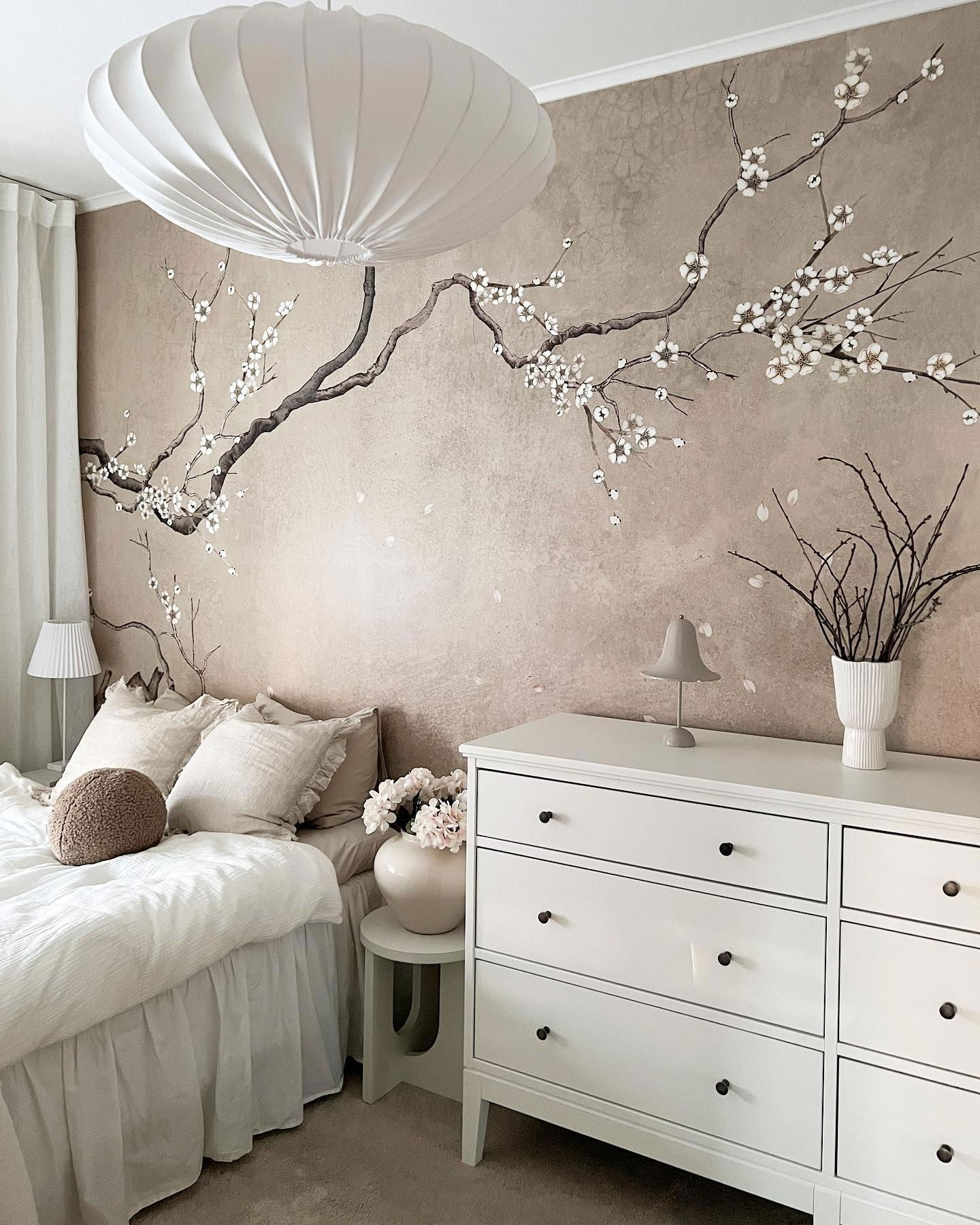 Bedroom with white bedding, dresser, and floral wall art. A large, white pendant light hangs above the bed.