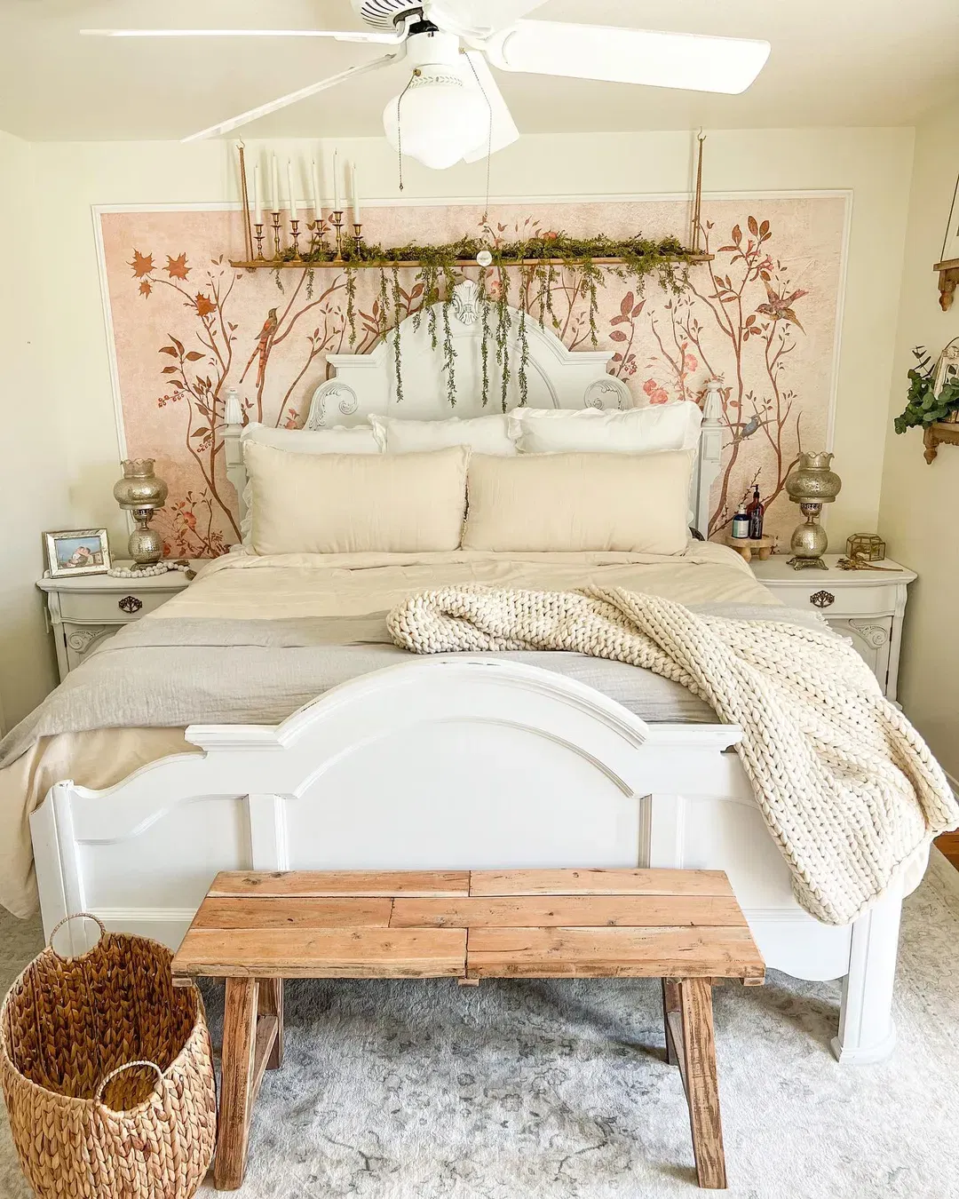 Camera da letto con letto bianco, carta da parati floreale e panca in legno. Un cesto intrecciato è posizionato su un tappeto grigio.