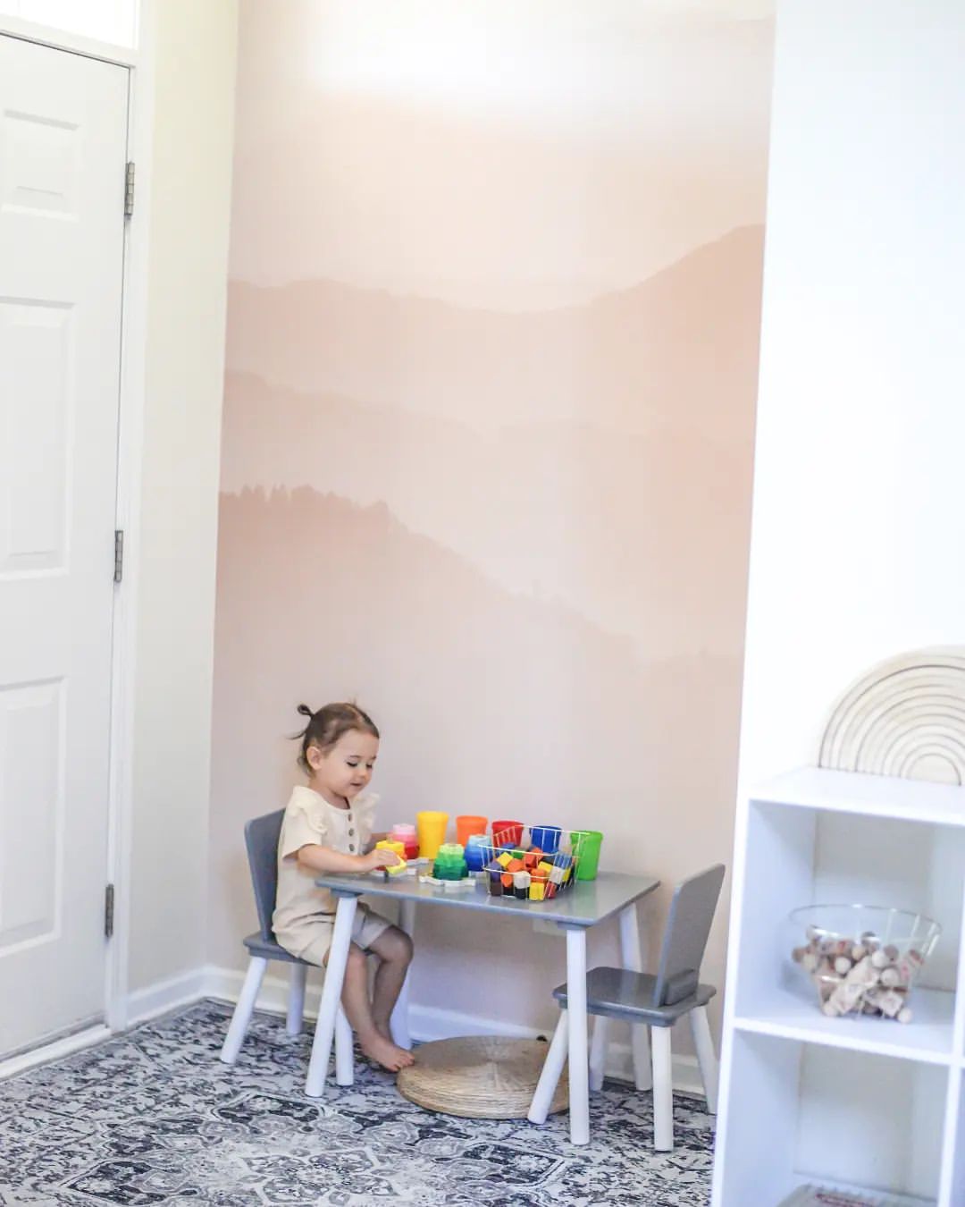 Een kind speelt met blokken aan een grijze tafel in een speelkamer met een bergmuurschildering.