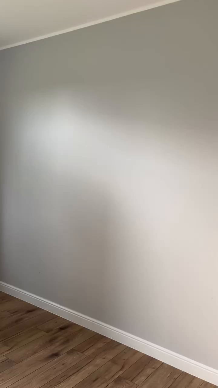 Interior shot of a gray wall with white trim and wood flooring.