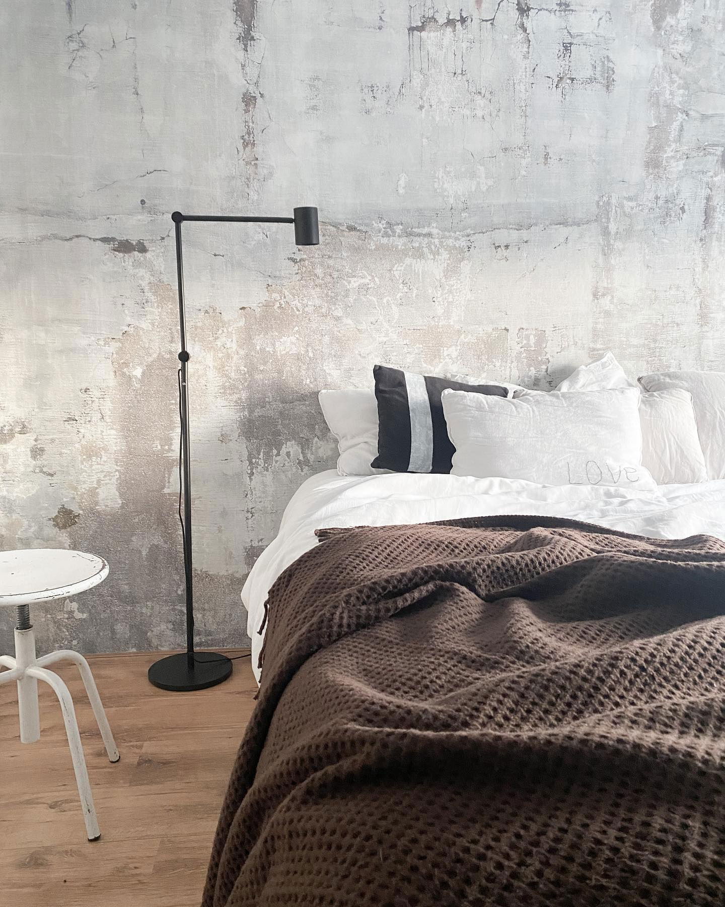 Slaapkamer met bruine wafelsprei, wit linnen en een muur met textuur.