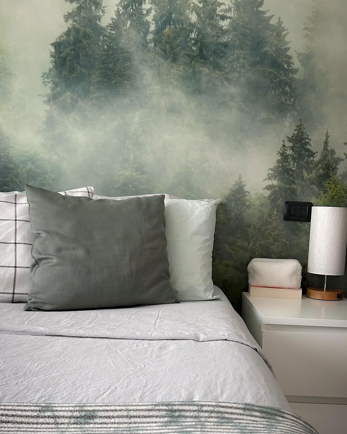 Schlafzimmer mit Waldtapete, grauen Kissen und weißem Nachttisch.