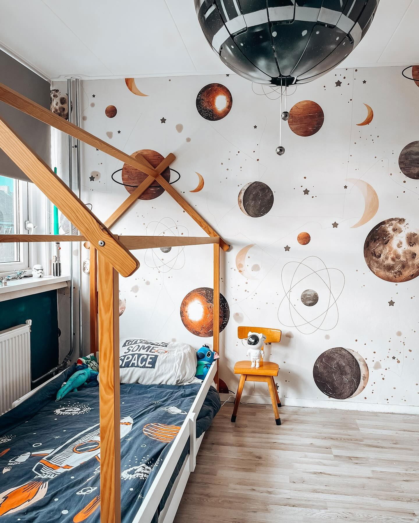 Kinderzimmer mit Weltraumthema. Planetentapete, Holzbettgestell und Raumschiff-Bettdecke.